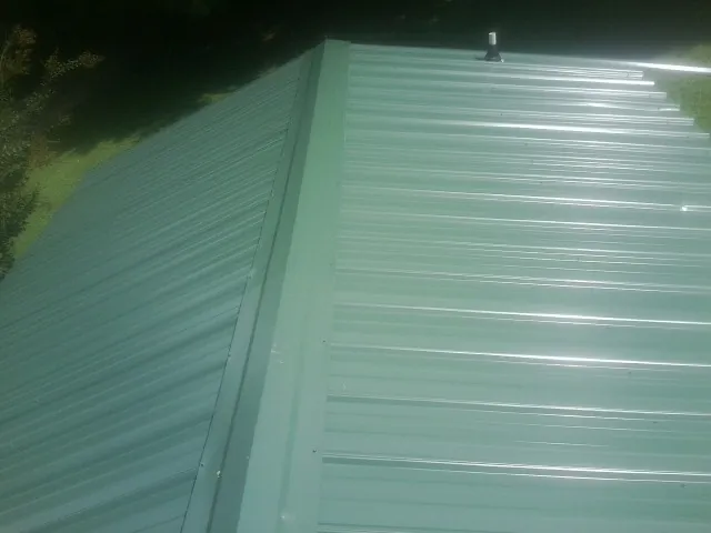 New green metal panels meeting at the ridge of a roof — Flat Roof Repair work by our crew in Somers